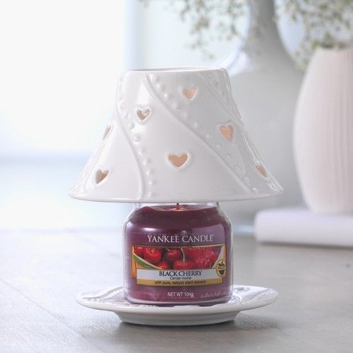 Yankee Candle Black Cherry kaars met witte keramische lampenkap. Kaars staat op een onderzetter. Achtergrond onscherp.