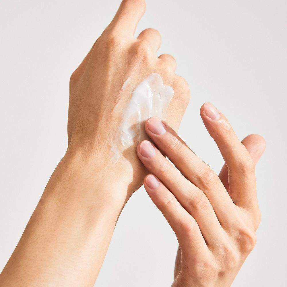 Handen die crème aanbrengen. Witte crème op de huid. Lichte huidskleur. Close-up.