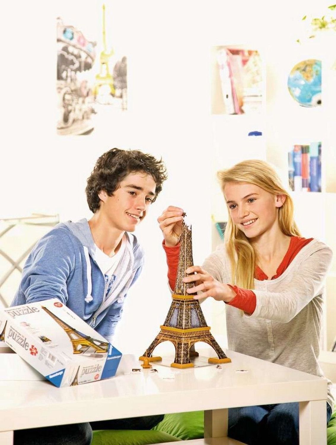 Twee tieners bouwen een 3D-puzzel Eiffeltoren. Puzzel en verpakking op een tafel. Lichte omgeving.