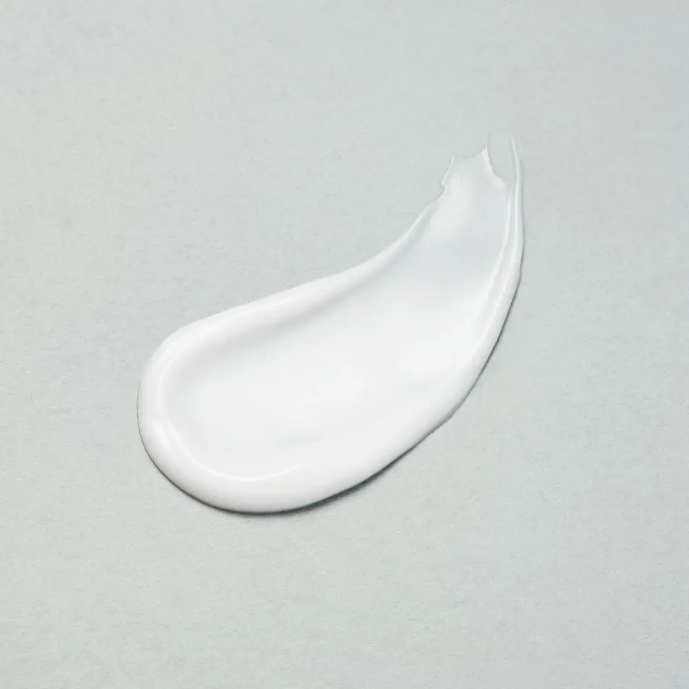 Vlek witte lotion op grijze achtergrond. Gladde textuur, licht glanzend.