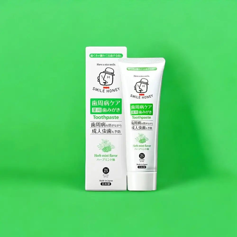 Witte tandpastatube en verpakking met groene en zwarte tekst. Opschrift: SMILE HONEY, Toothpaste, Herb mint flavor.