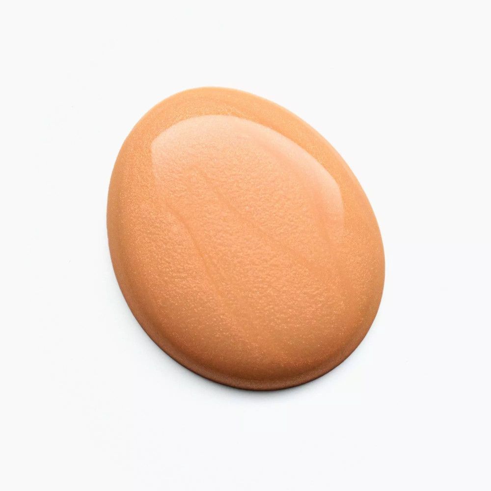 Une tache ovale de vernis à ongles orange clair sur fond blanc. Surface brillante.