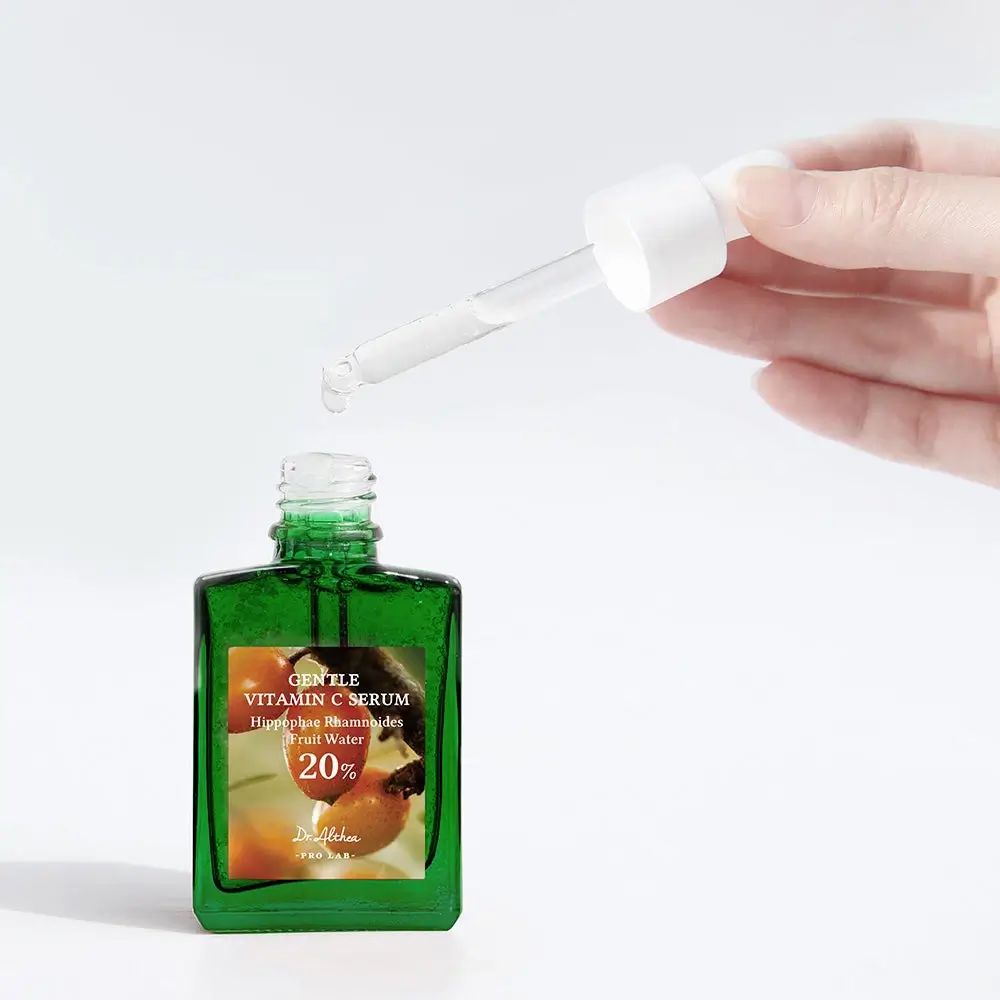 Flacon en verre vert avec pipette. Main tenant la pipette au-dessus du flacon ouvert. Inscription : Gentle Vitamin C Serum.