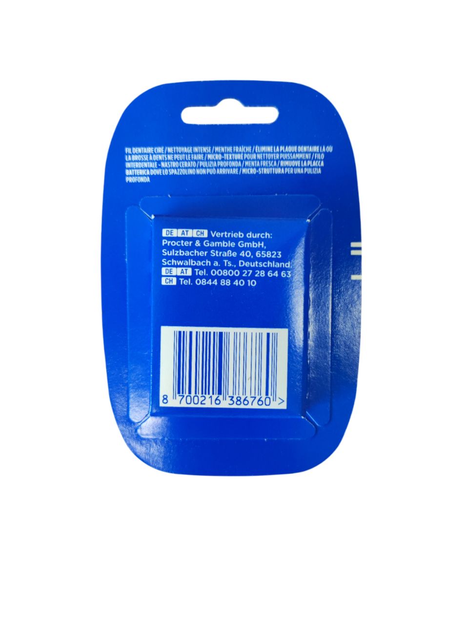 Achterkant van de tandflosverpakking. Blauwe verpakking met tekst en barcode. Fabrikantinformatie.