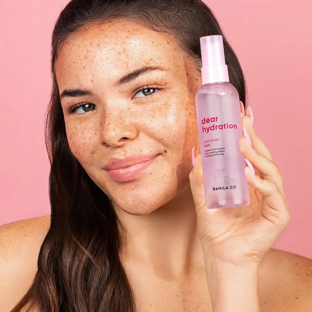 Vrouw houdt een roze spuitfles vast. Opschrift: dear hydration cool down mist. Merk: BANILA CO.