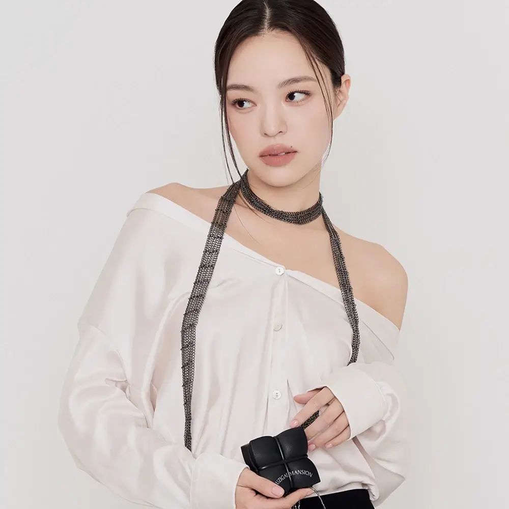 Vrouw in witte top en zwarte broek. Ze houdt een zwarte, vierkante etui vast.