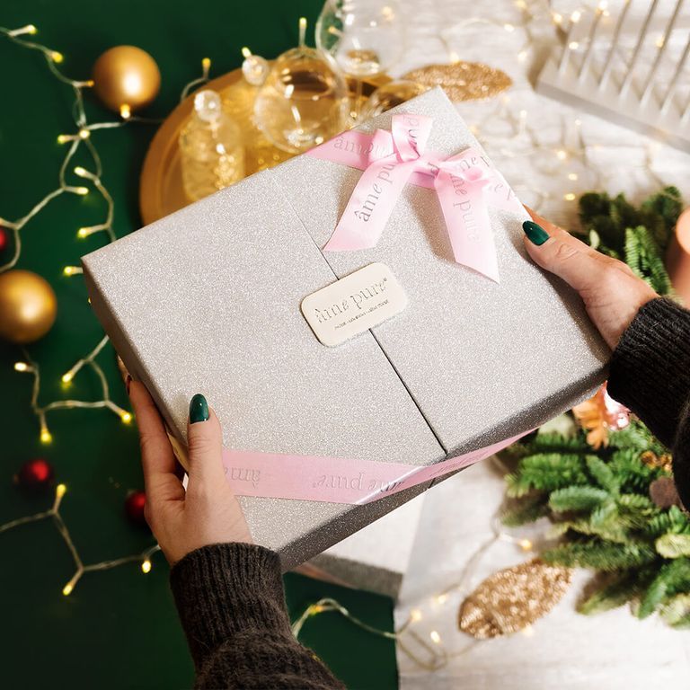 Een glinsterende geschenkdoos met roze linten, "âme pure" logo op een label.