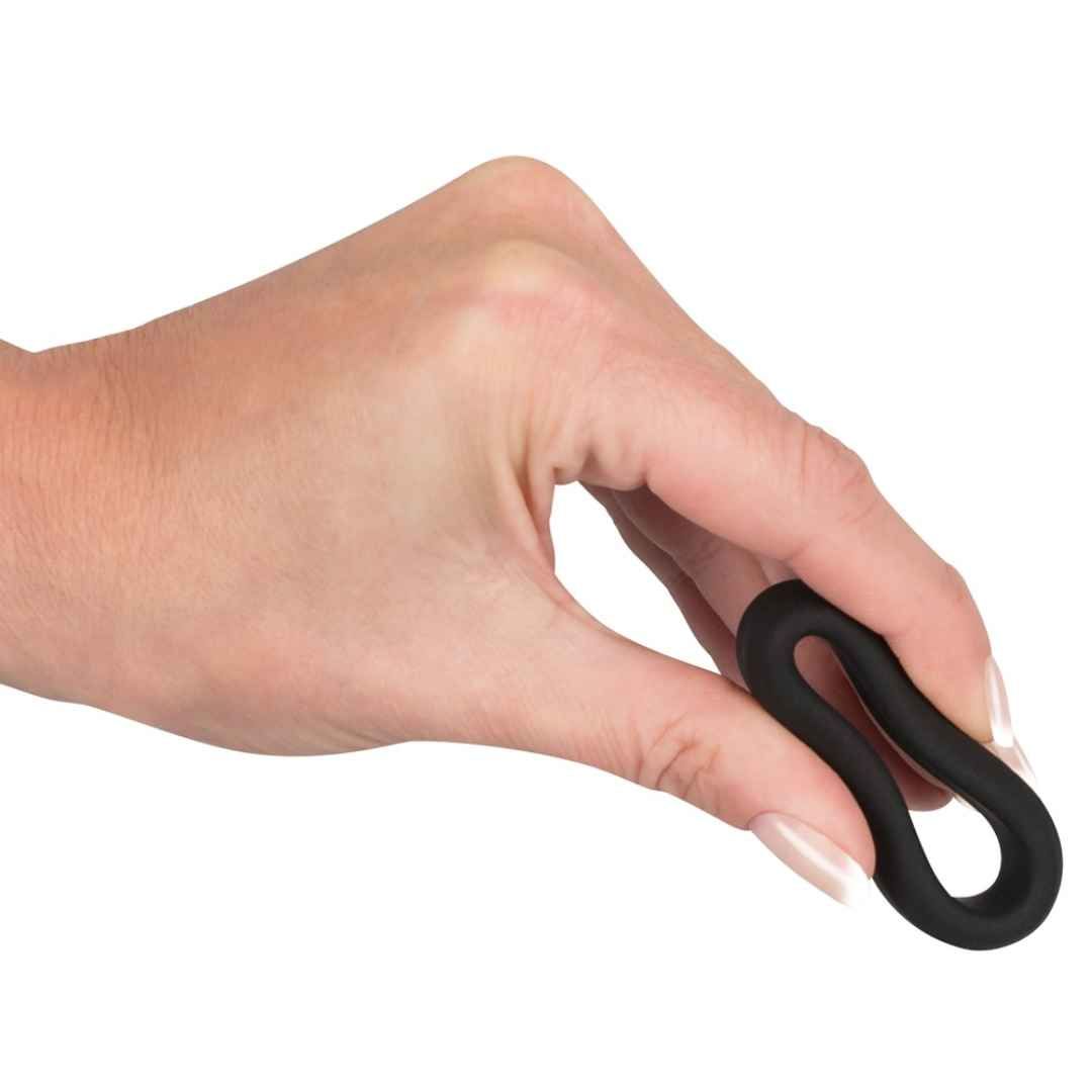 Main tenant une bague de pénis noire flexible en silicone.