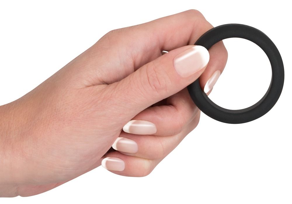 Anneau noir et souple en silicone, tenu par une main aux ongles soignés.