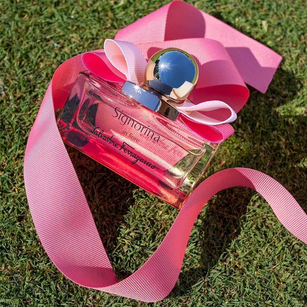 Flacon en verre rose sur l'herbe. Bouchon doré, nœud rose. Inscription Signorina in fiore et Salvatore Ferragamo.