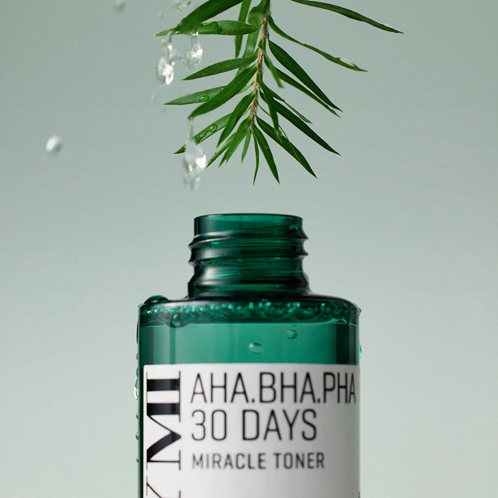 Groene fles met witte tekst. Druppels vallen op de fles. Een groene tak erboven.