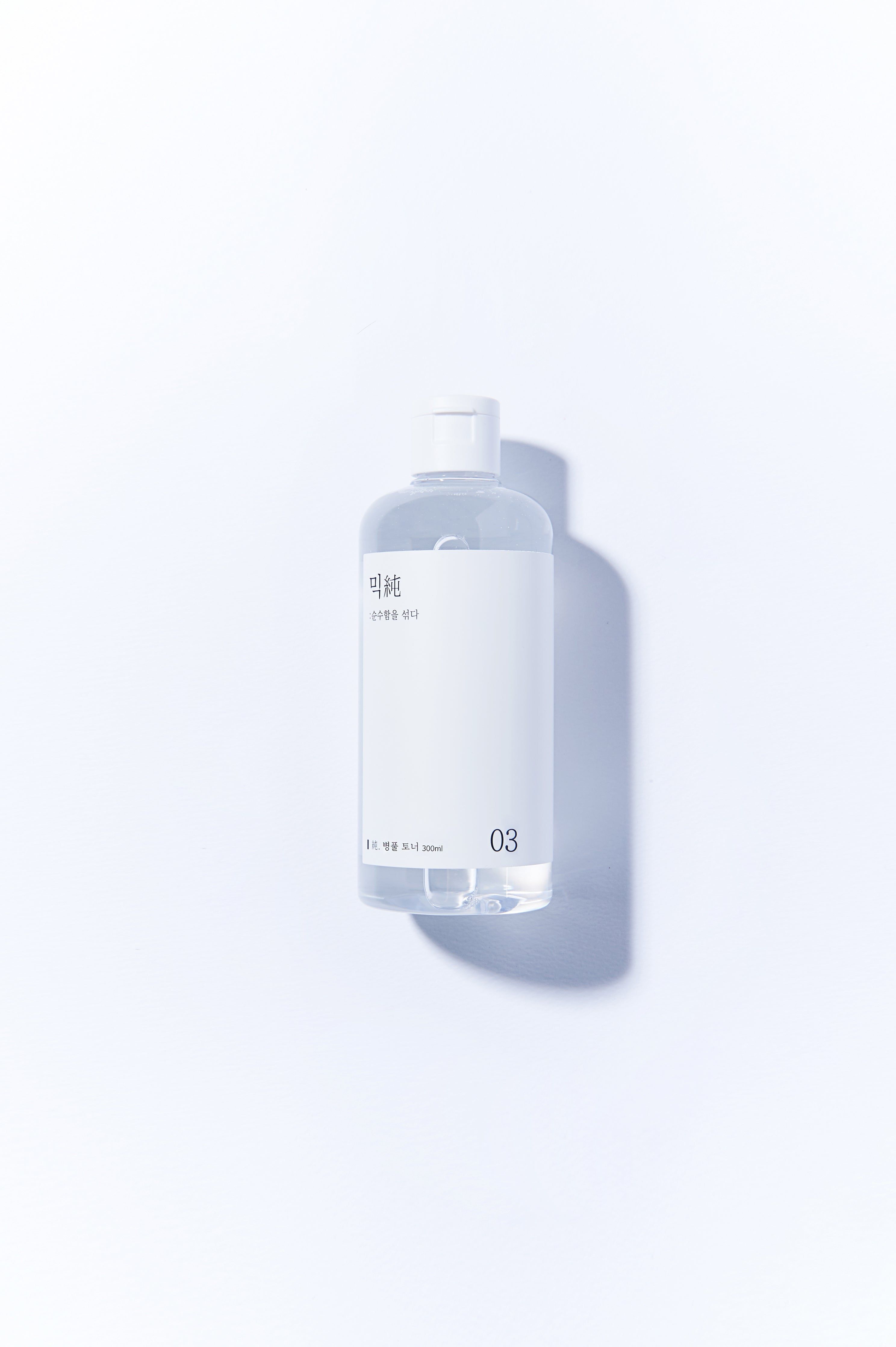 Flacon transparent avec bouchon blanc et étiquette. Inscription en coréen et le chiffre 03. Inscription: 200ml.