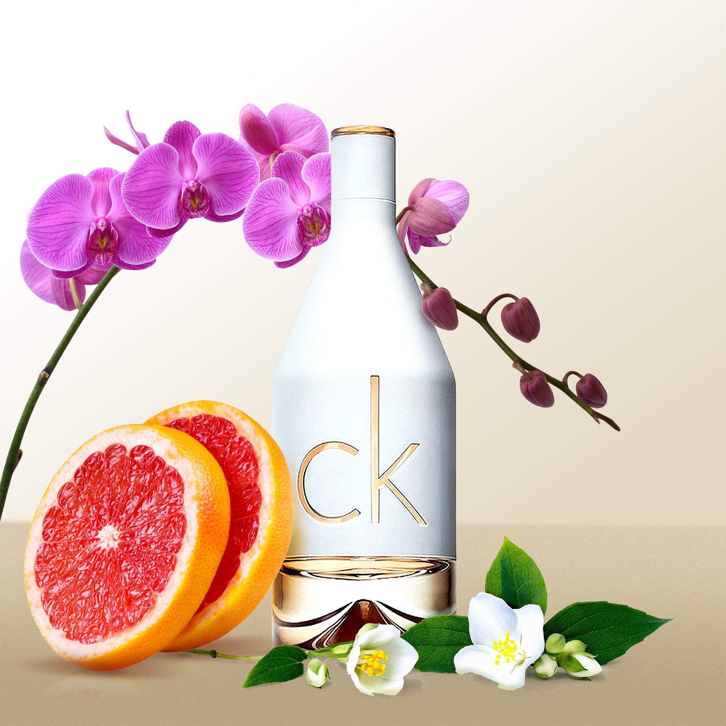 Flacon de parfum blanc avec logo "ck" doré. Décoré avec pamplemousse, orchidées et fleurs de jasmin.