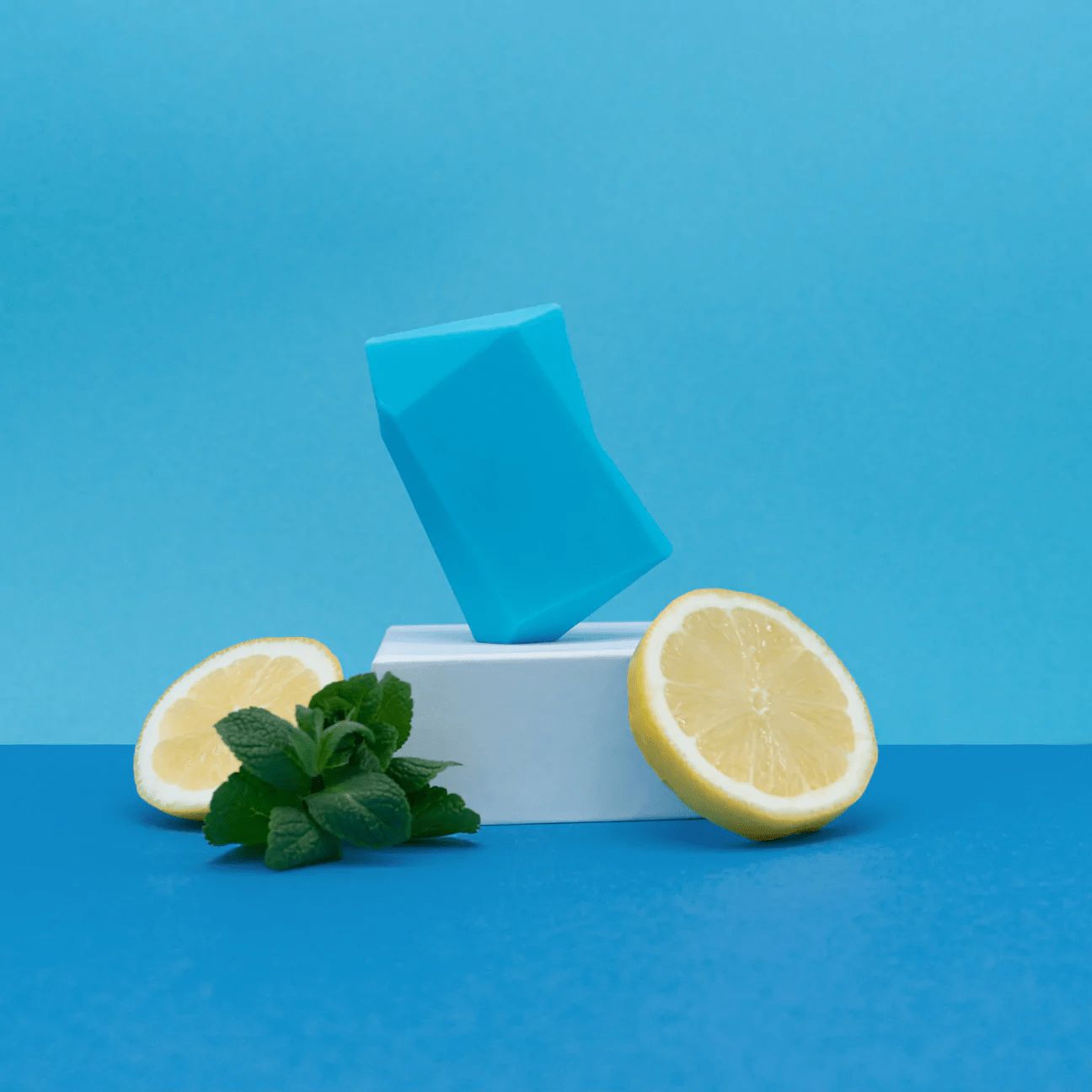 Duschbrocken turquoise sur socle blanc. Moitiés de citron et menthe sur fond bleu.