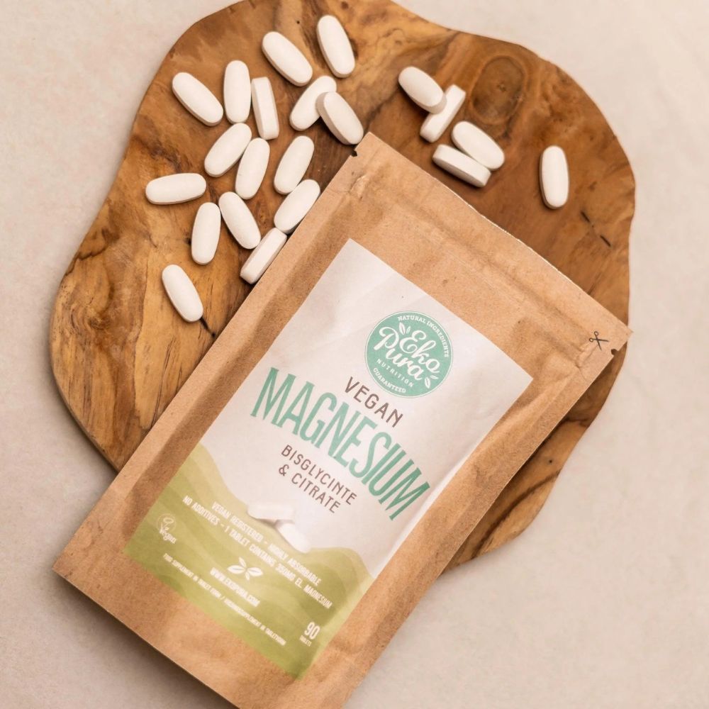 Bruine verpakking met wit etiket. Op het etiket staat "Vegan Magnesium". Tabletten liggen op een houten plank.