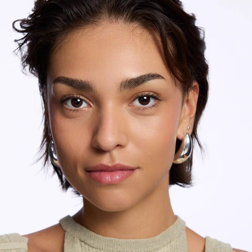 Portrait d'une femme aux cheveux courts et foncés, portant des boucles d'oreilles argentées. Lèvres légèrement maquillées.