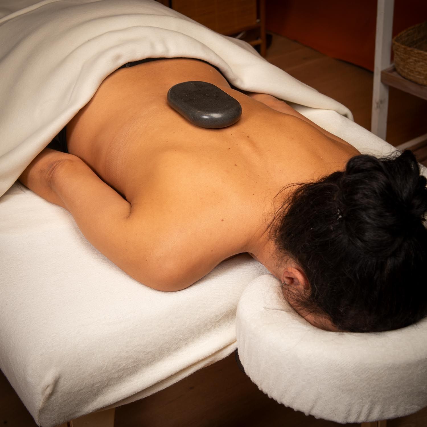 Grosse pierre ovale sur le dos d'une personne. La personne est allongée sur une table de massage, recouverte d'un drap blanc.