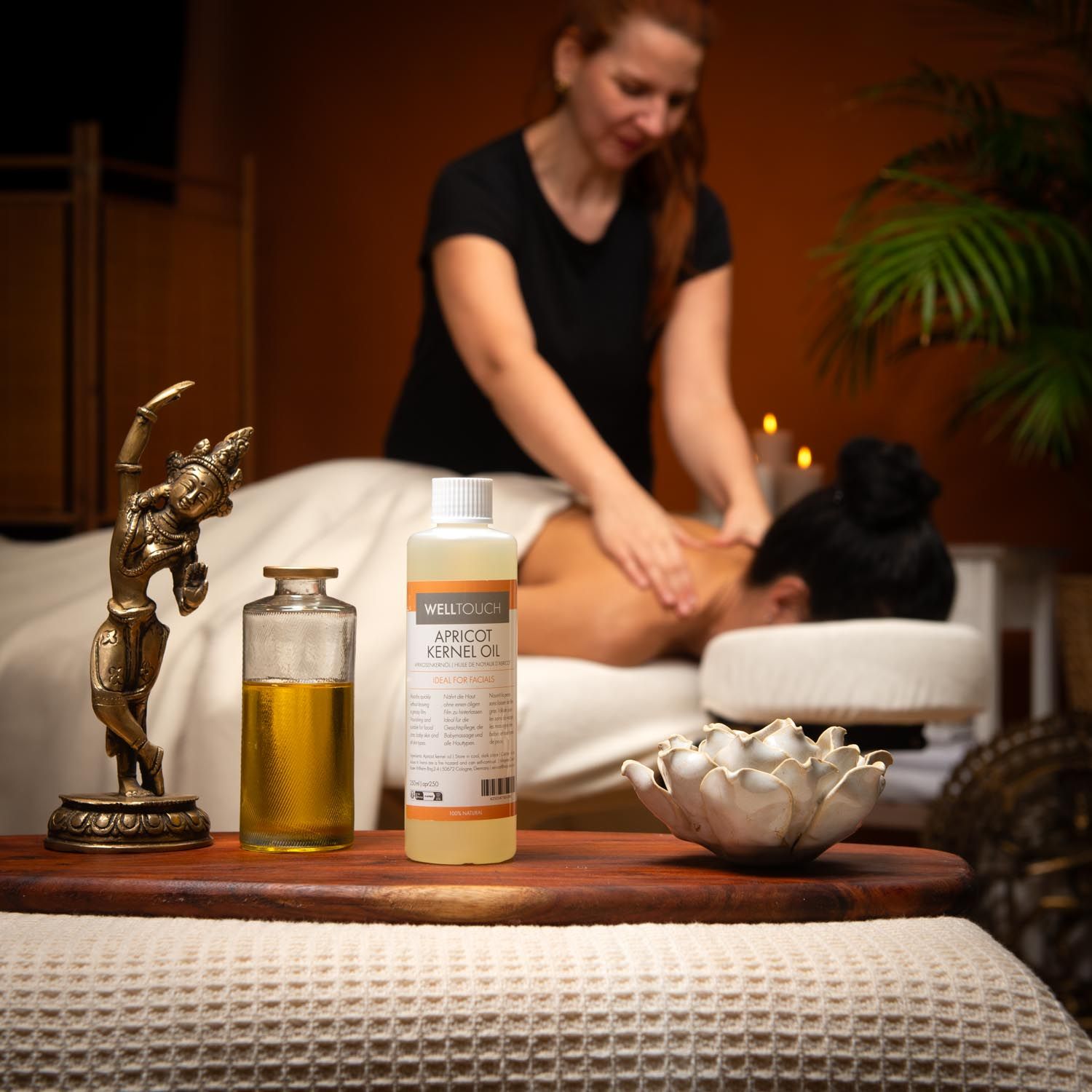 Welltouch abrikozenpitolie fles en glazen fles op houten dienblad. Vrouw krijgt massage. Decoratie.