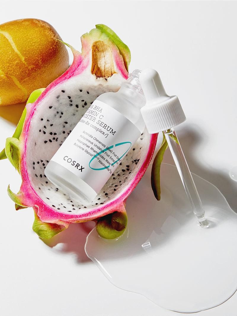 Flacon de sérum avec pipette dans un fruit du dragon. Inscription : AHA BHA Vitamin C Booster Serum. Marque : COSRX.