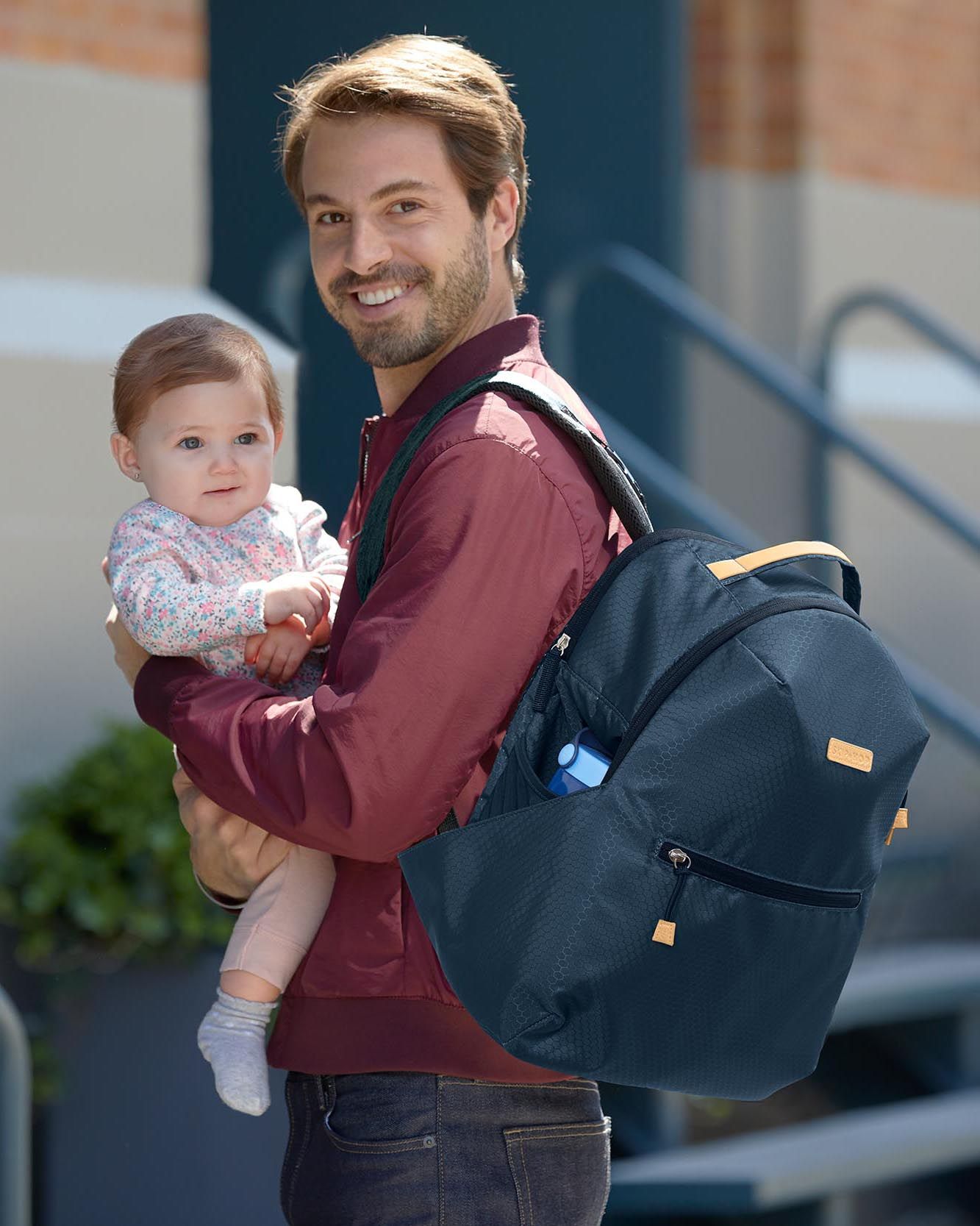 Donkerblauwe luiertas op de rug van een man die een baby vasthoudt. Gele accenten.