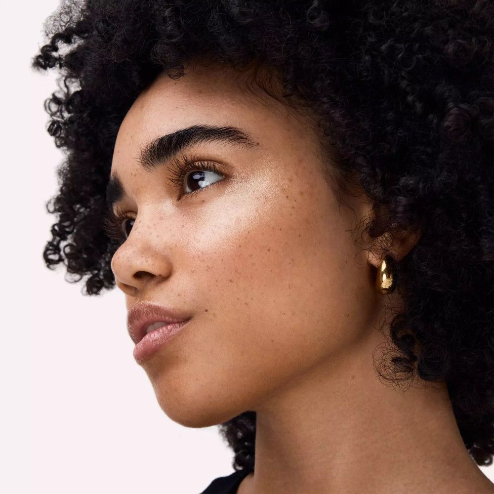 Portret van een vrouw met sproeten. Ze draagt gouden oorringen en heeft highlighter aangebracht.