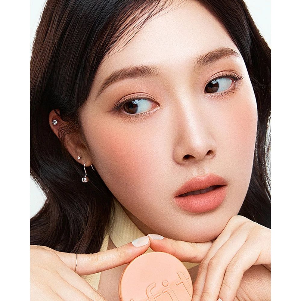 Een vrouw houdt een perzikroze TFIT Fluffy Velvet Cushion Blush vast. Het product is op haar wangen aangebracht.