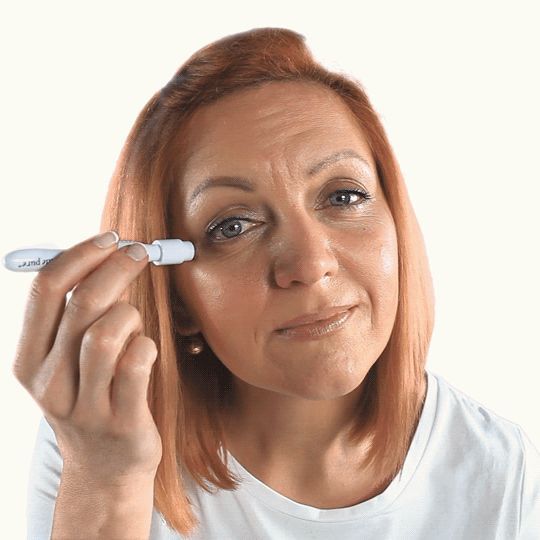 Een vrouw met rood haar gebruikt een huidroller bij haar oog.