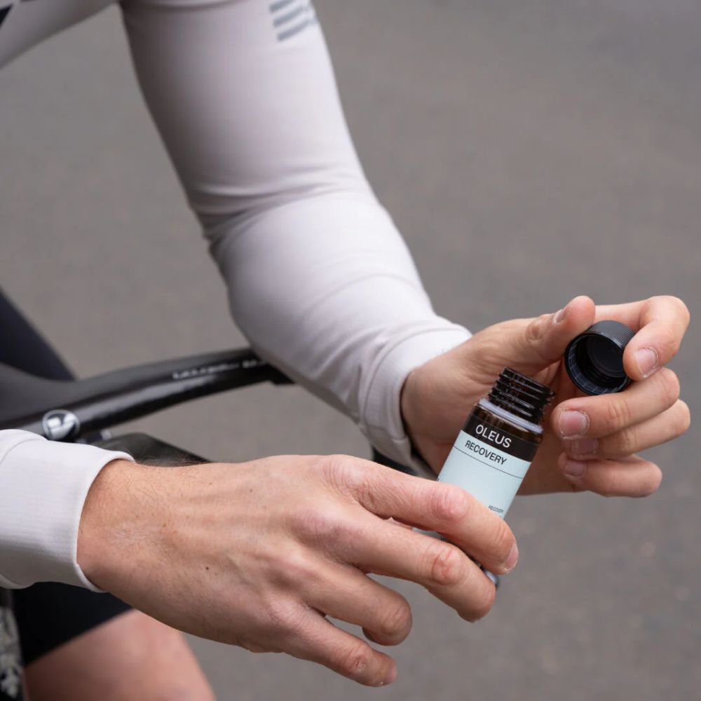 Persoon houdt een fles OLEUS RECOVERY vast. Fiets op de achtergrond.