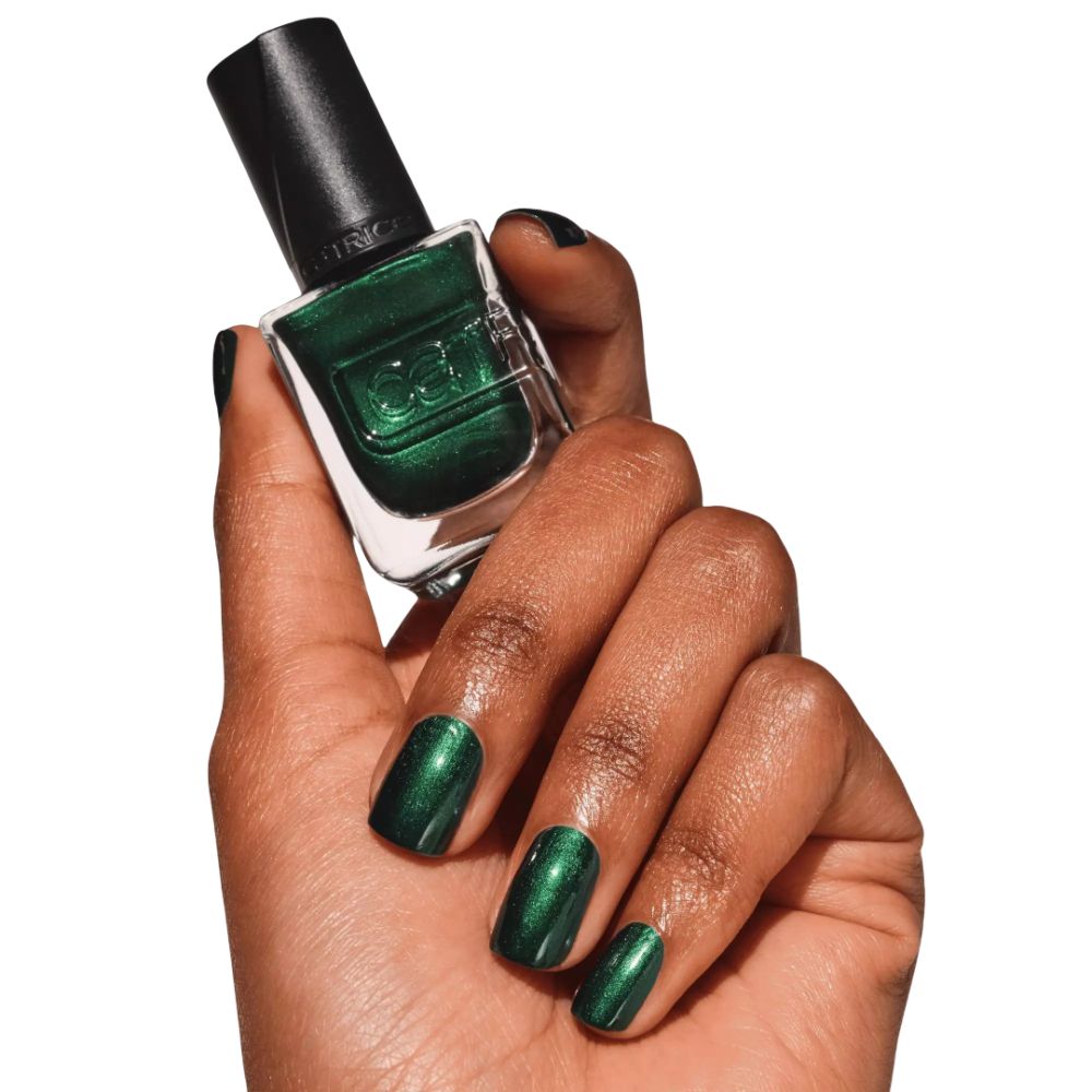 Main avec ongles vernis en vert tenant un flacon de vernis. Marque Catrice visible. Ongles et flacon verts.