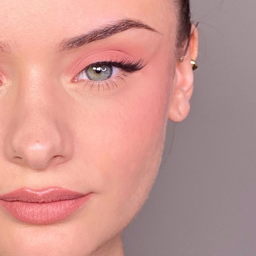 Gros plan d'un visage maquillé de rose sur les yeux et les joues. Yeux verts, boucle d'oreille dorée.