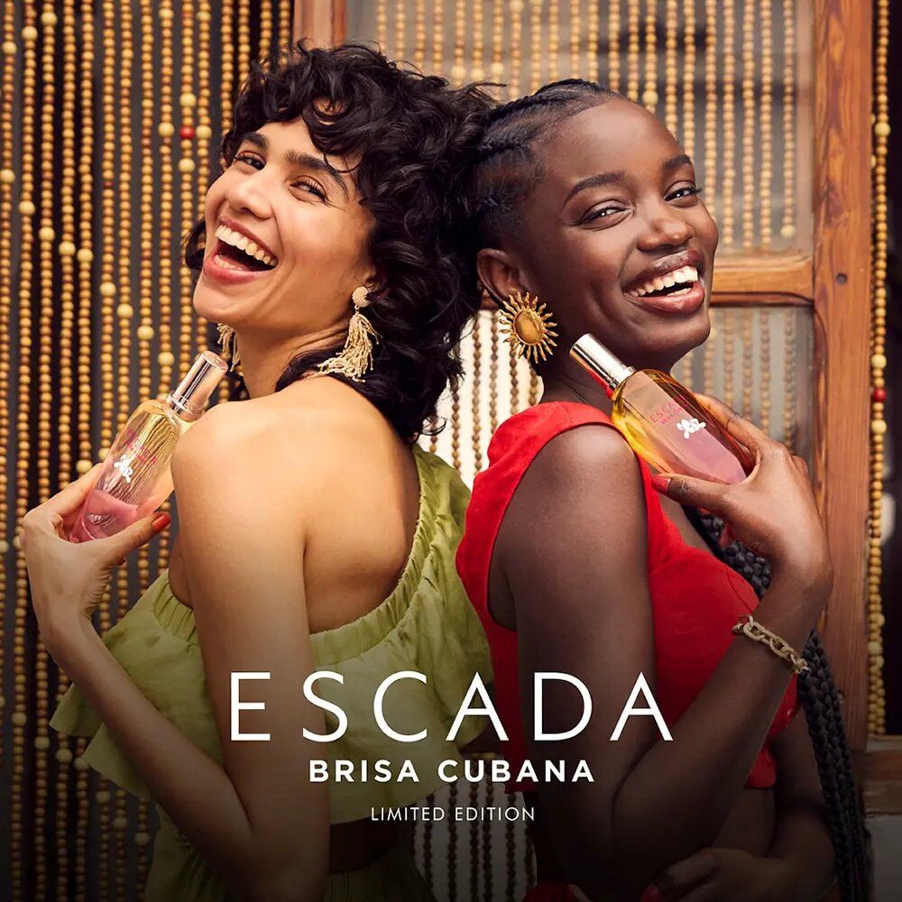Twee vrouwen houden Escada Brisa Cubana parfumflesjes vast. Opschrift: Escada Brisa Cubana Limited Edition. Beide lachen.