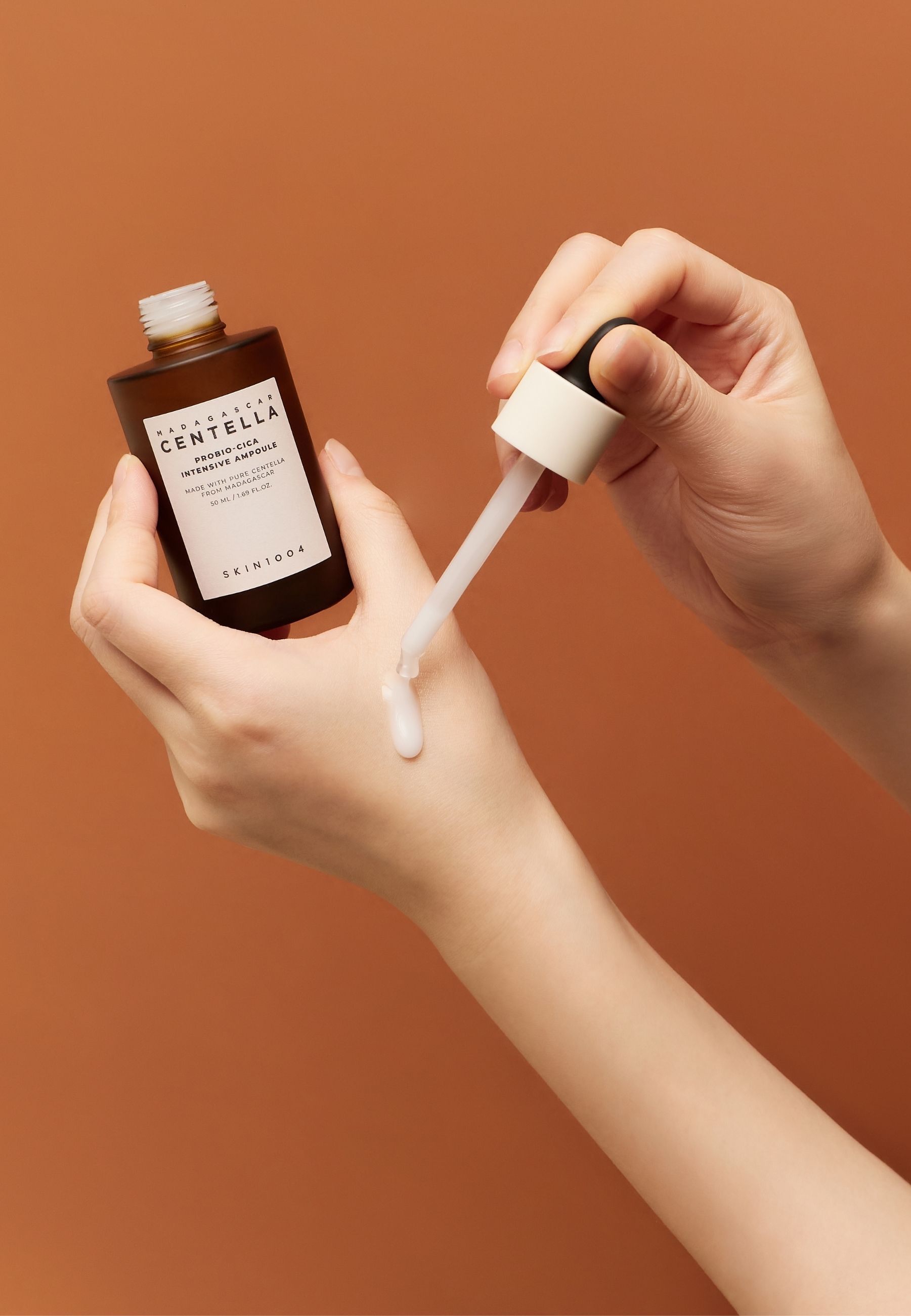 Handen houden fles en pipet. Serum wordt op de hand aangebracht. Achtergrond: oranje.