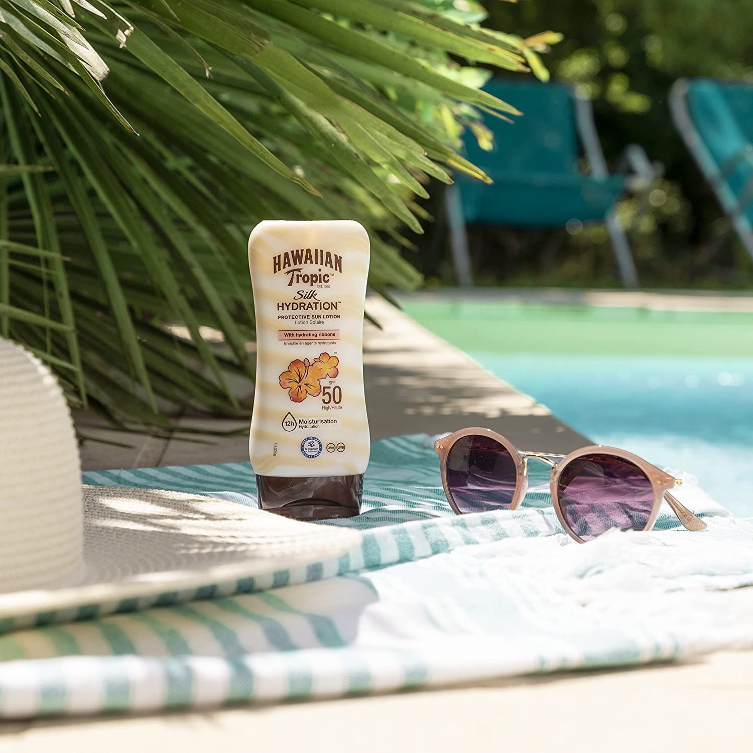 Lotion solaire près de lunettes de soleil et serviette au bord de la piscine. Hawaiian Tropic, SPF 50.