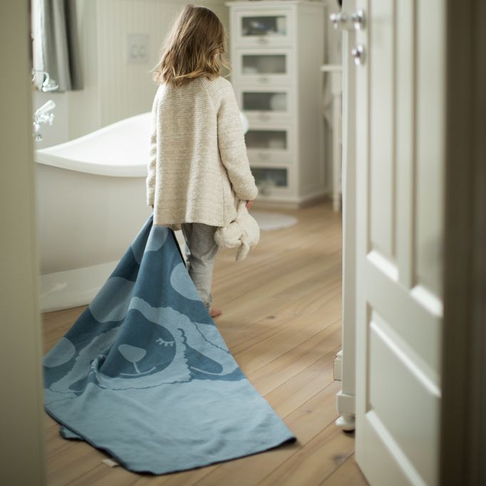 Kind met blauwe schapenplaid in de hand, loopt door een deur. Badkamer op de achtergrond.