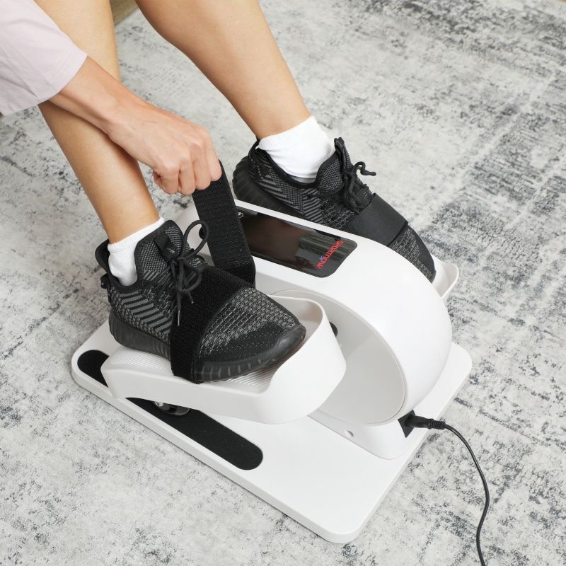 Close-up: voeten in zwarte schoenen op mini-elliptische trainer. Zwarte banden. Persoon maakt banden vast.