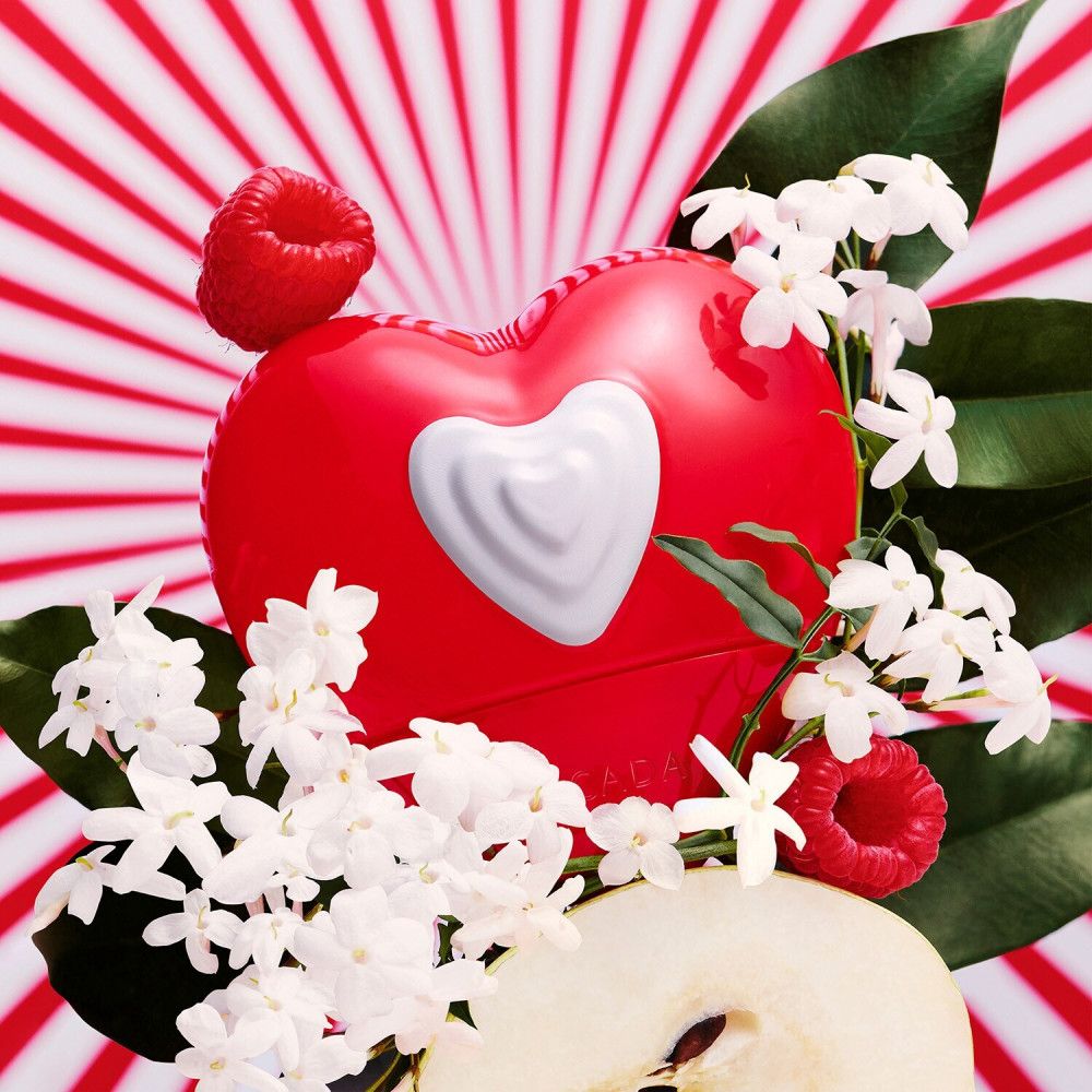 Flacon rouge en forme de cœur avec un cœur blanc. Décoré de fleurs de jasmin, de framboises et d'une tranche de poire. Fond rayé rouge.