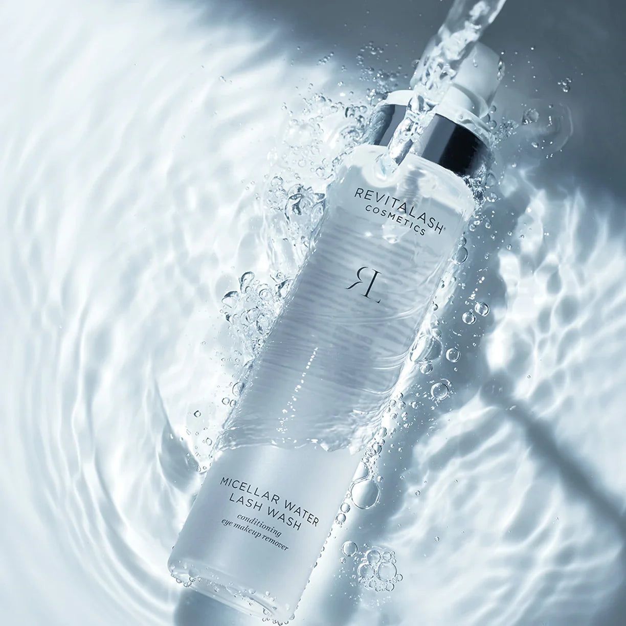 Flacon transparent avec vaporisateur, entouré d'eau. Inscription: RevitaLash Cosmetics, Micellar Water Lash Wash.
