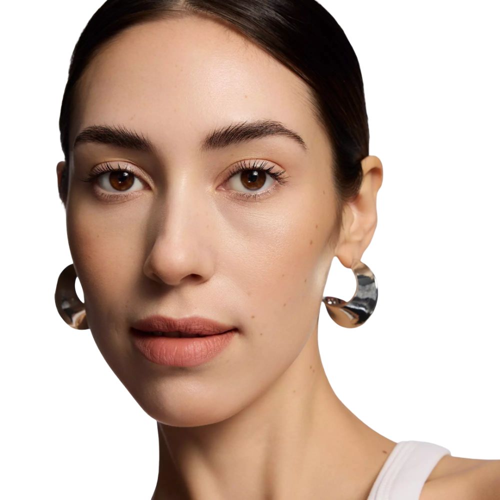 Gros plan d'une femme avec des lèvres brun clair. Elle porte des boucles d'oreilles argentées.