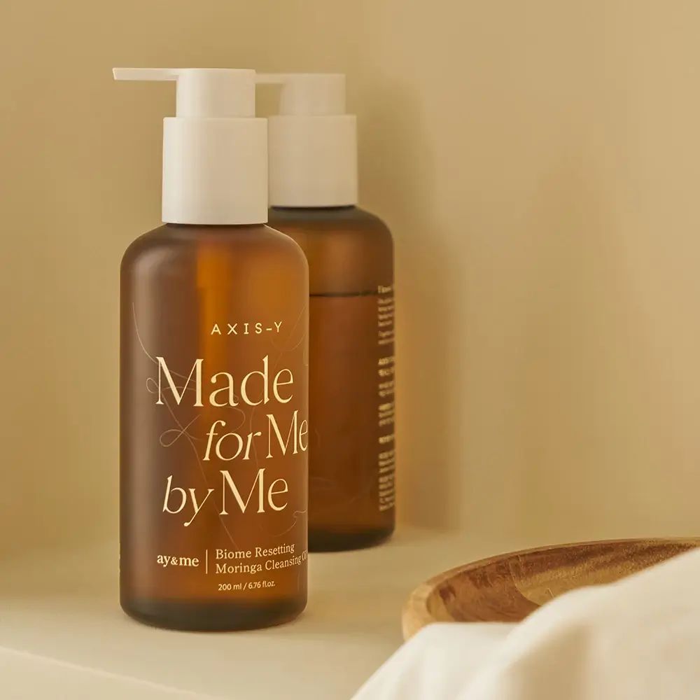 Twee bruine flessen met witte pompen. Opschrift: AXIS-Y, Made for Me by Me, Biome Resetting Moringa Cleansing Oil.