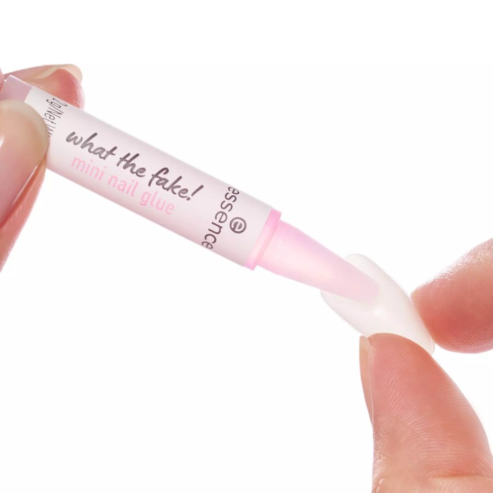 Applicateur de colle à ongles, blanc avec embout rose, tenant un faux ongle. Inscription 'what the fake!'.