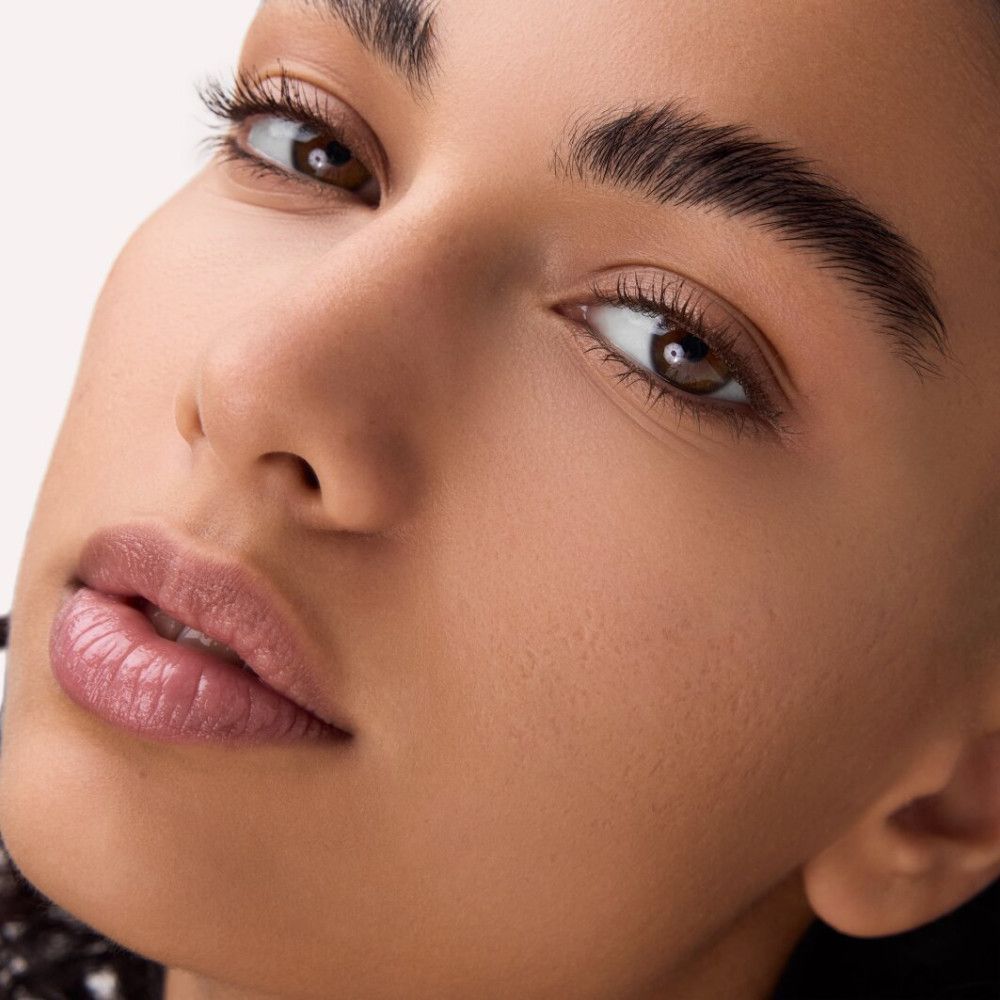 Gros plan d'un visage maquillé. Accent sur les yeux et les lèvres. Teint et texture de la peau visibles.