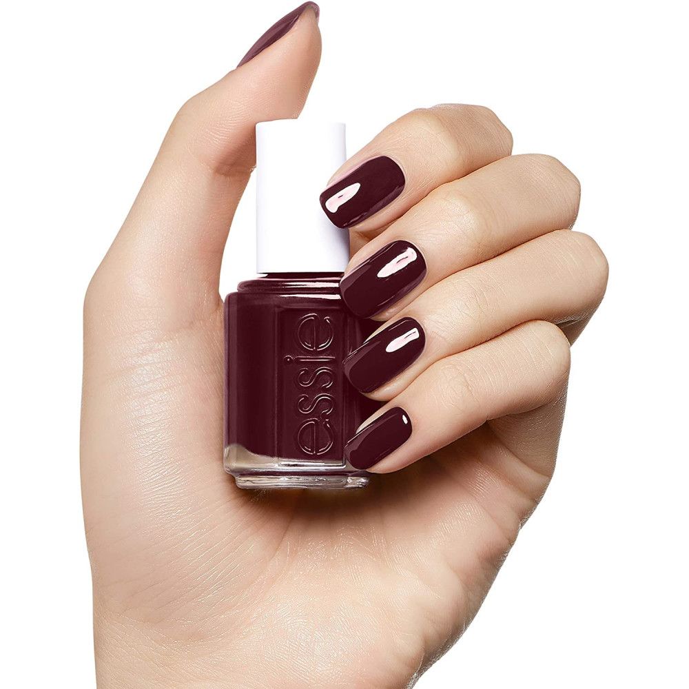 Essie nagellakfles en donkerrood gelakte nagels. Fles met witte dop, vastgehouden door een hand.