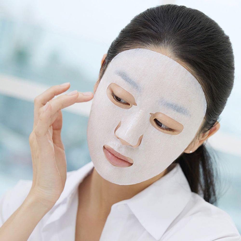 Une femme portant un masque facial blanc, touchant doucement son visage.