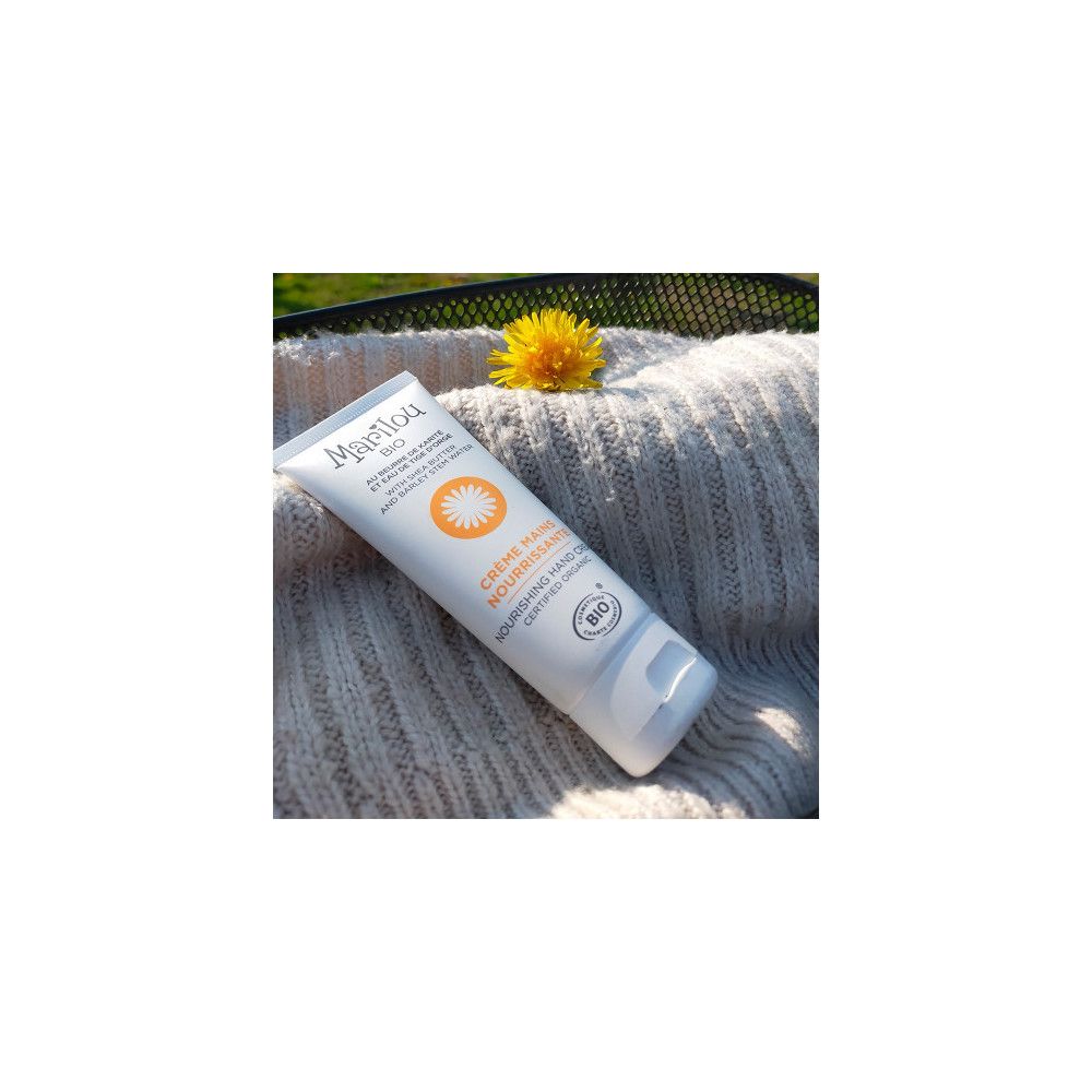 Tube de crème pour les mains Marilou Bio. Posé sur un pull gris, avec une fleur.