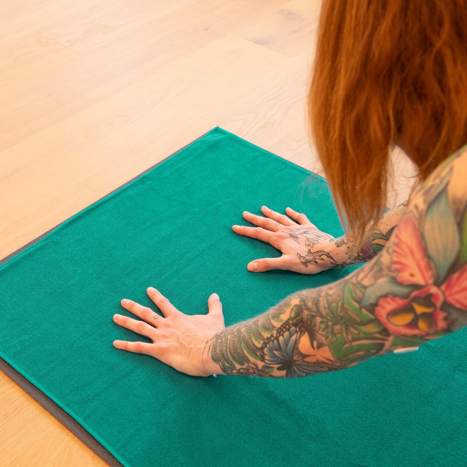 Personne avec des tatouages sur une serviette de yoga verte. Mains sur la serviette.
