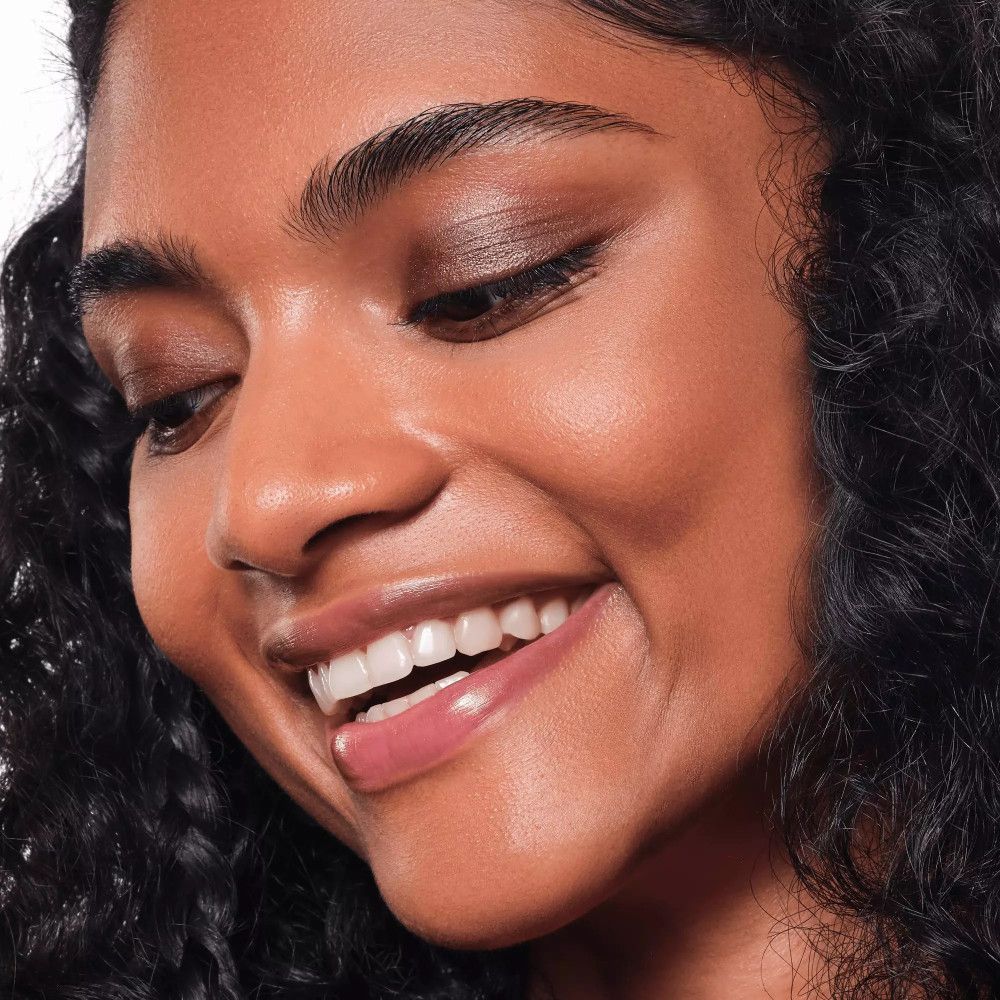 Femme avec de l'ombre à paupières crème sur les yeux. Elle sourit.