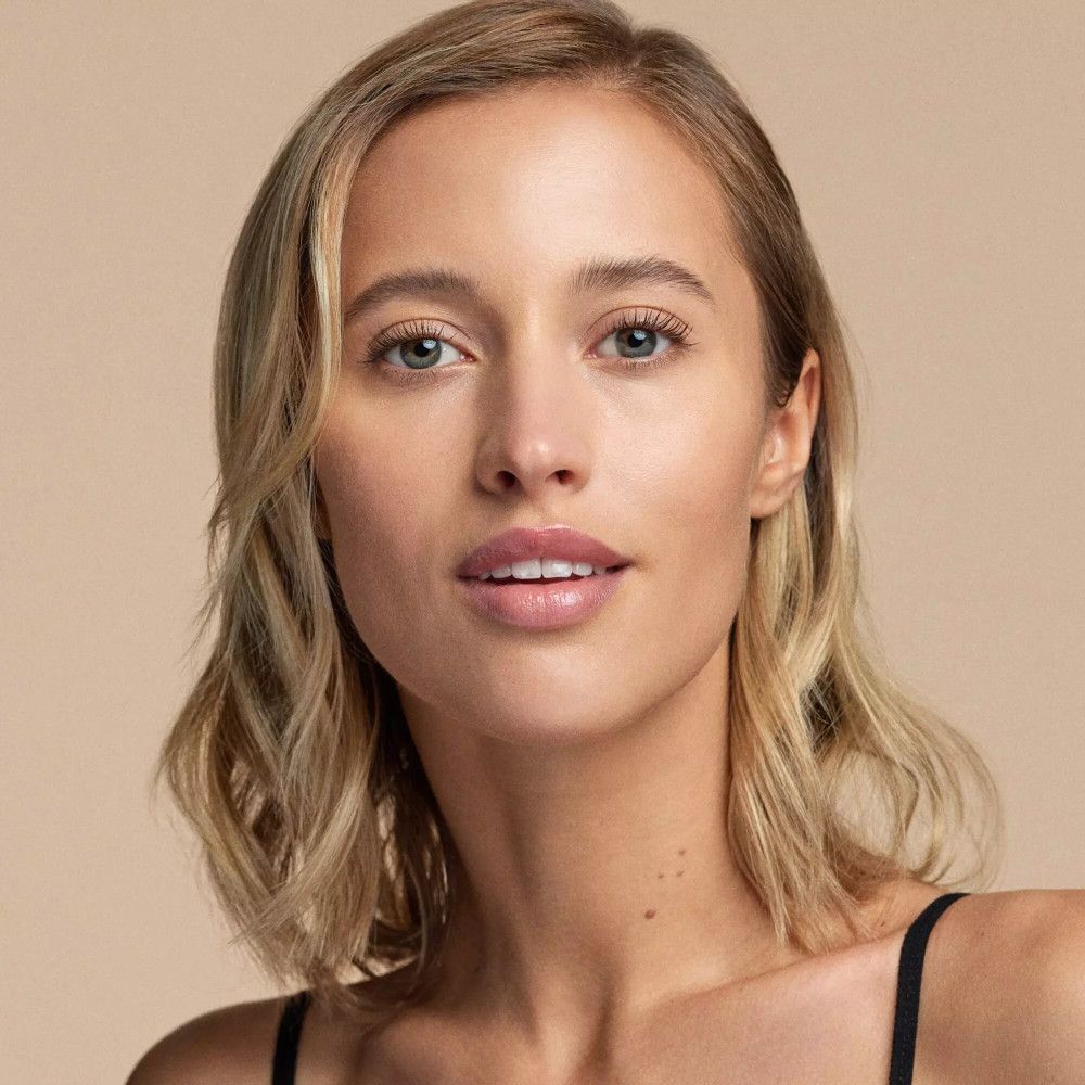 Portrait d'une femme à la peau claire et aux cheveux blonds. Elle porte un haut noir. Fond: marron clair.