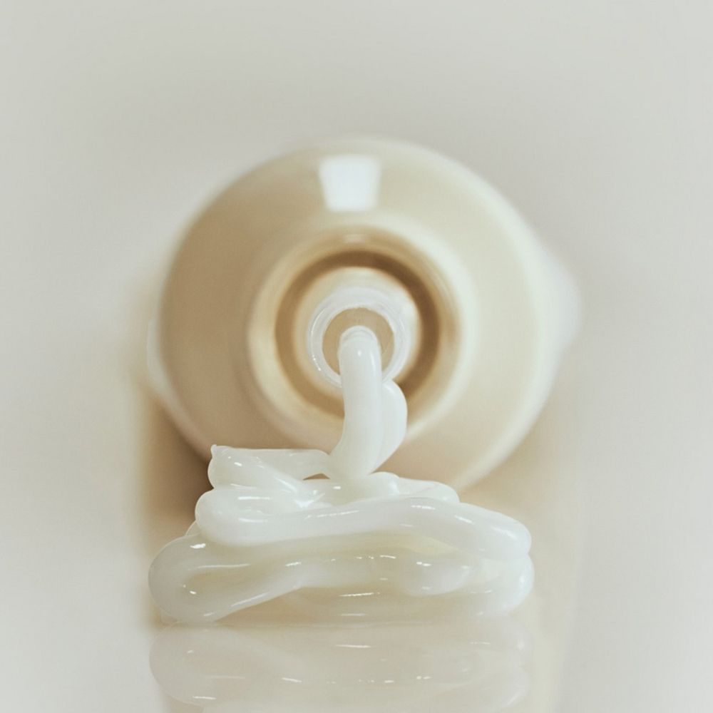 Close-up: crème komt uit een lichtbeige tube. Op lichte achtergrond. Crèmetube ligt.