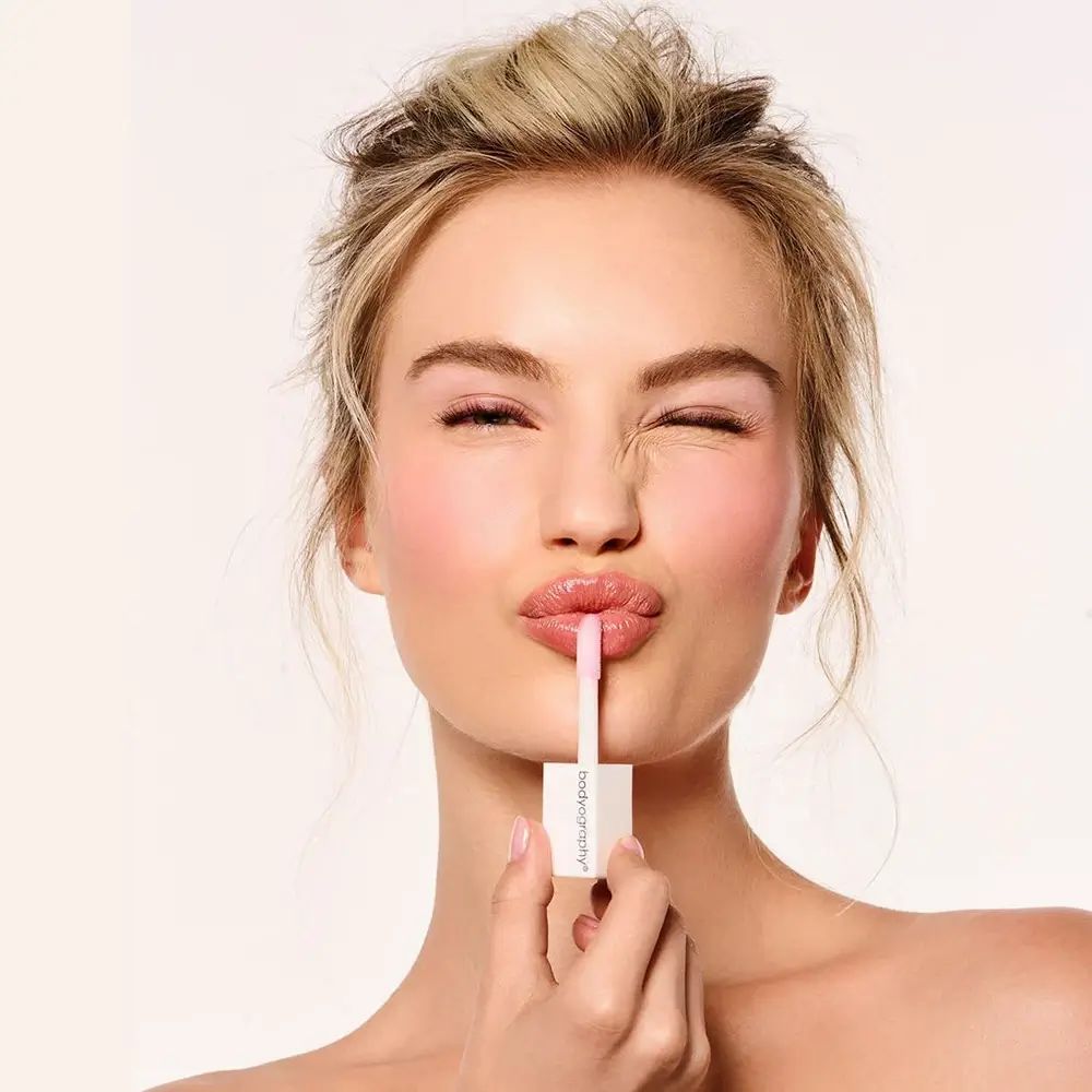 Vrouw houdt lipgloss applicator op haar lippen. Bodyography staat op de dop.
