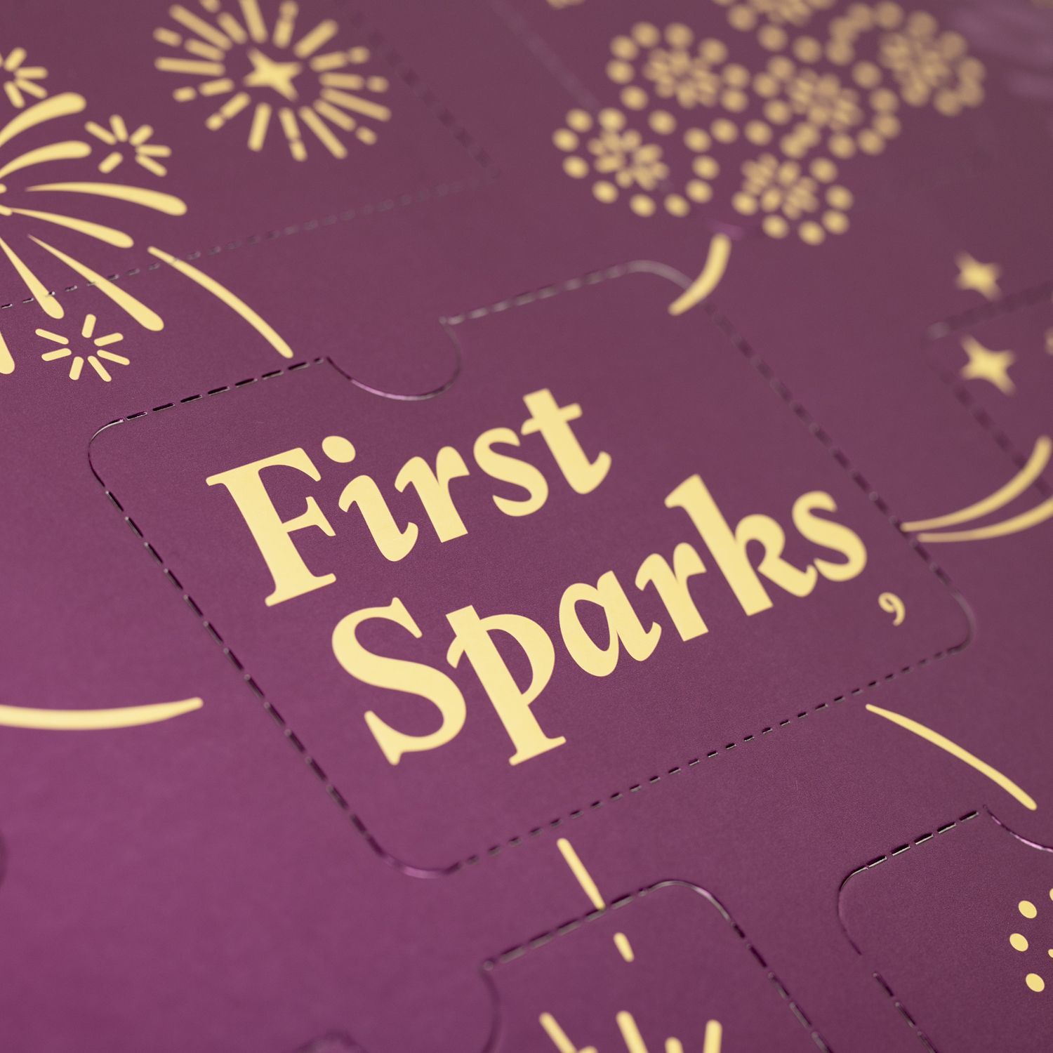 Close-up van de adventskalender. Gouden tekst: First Sparks. Illustraties van vuurwerk.